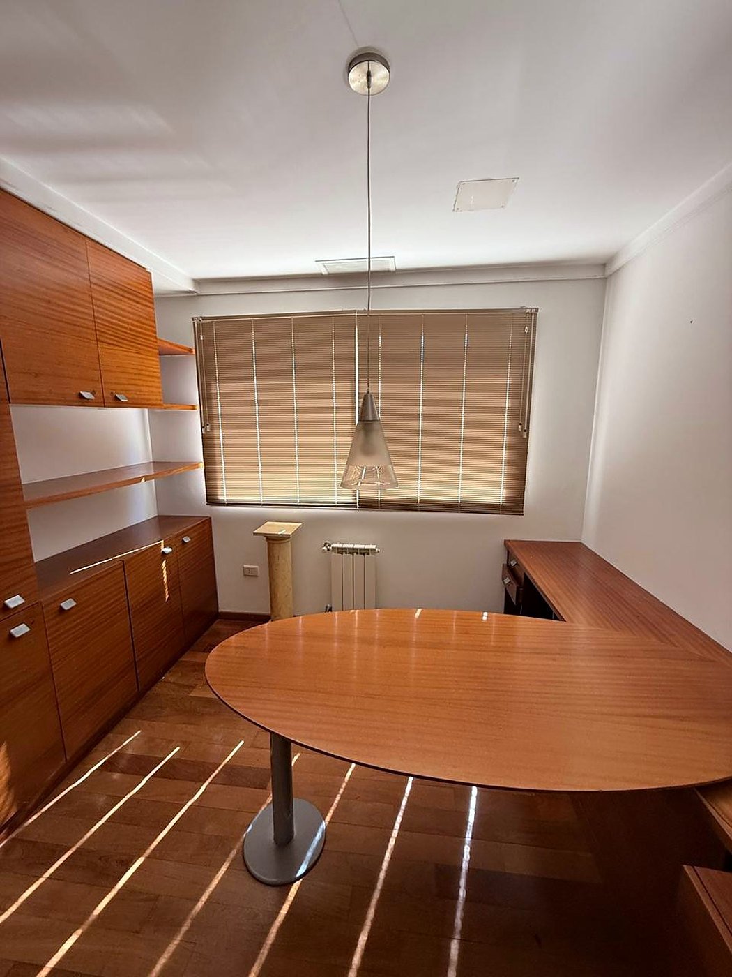 Fitted home office with wood veneer wall units, shelving and an oval desk joined to the worktop